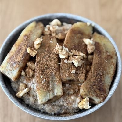 Porridge mit längs halbierter, gebratener Banane, Zimt und Walnüssen