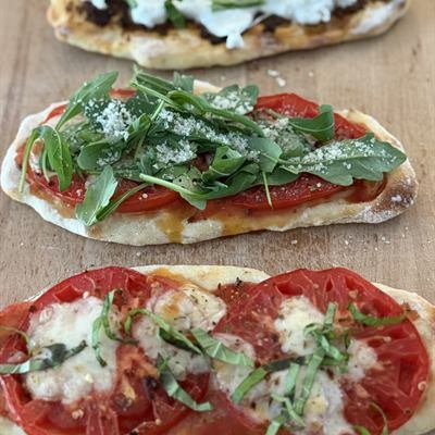 Drei Pizza-Flatbreads mit Tomaten, Mozzarella und Basilikum auf einem Holzbrett