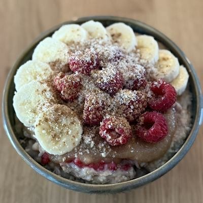 Porridge mit Bananenscheiben, Himbeeren, Apfelmus und gemahlenen Mandeln