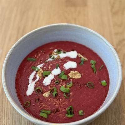 Pinke Rote-Bete-Suppe mit einem Klecks Sahne und Frühlingszwiebeln