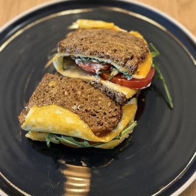 Sandwich mit Rührei, Tomate und Rucola auf einem dunklen Teller